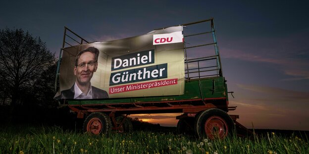 Ein Plakat des CDU-Kandidaten und Ministerpräsidenten Daniel Günther, befestigt an einem Heuwagen auf einer Wiese