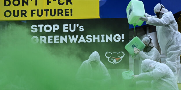 Menschen in Schutzkleidung mit Atomfässern in grünem Nebel vor Schild "Don't f+ck our Future""
