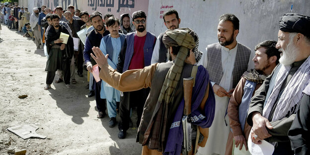 Ein bewaffneter Taliban bewacht eine Menschenschlange