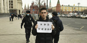 Junger Mann hält vor dem Kreml ein Blatt Papier mit Sternchen hoch. Polizist schreitet heran