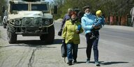 Zwei evakuierte Frauen mit Kleinkind gehen auf der Straße vor einem Militärfahrzeug