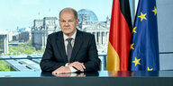 Bundeskanzler Olaf sitzt mit eernster Miene vor der deutschen und europäischen Flagge