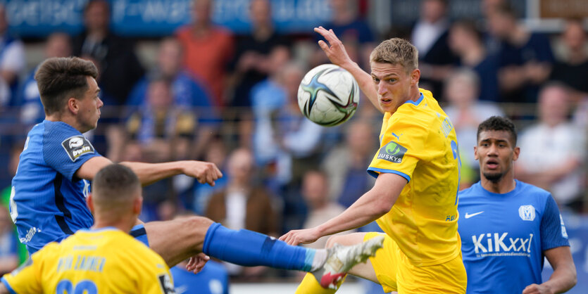 Fußballspieler in gelben und blauen Trikots springen nach einem Ball