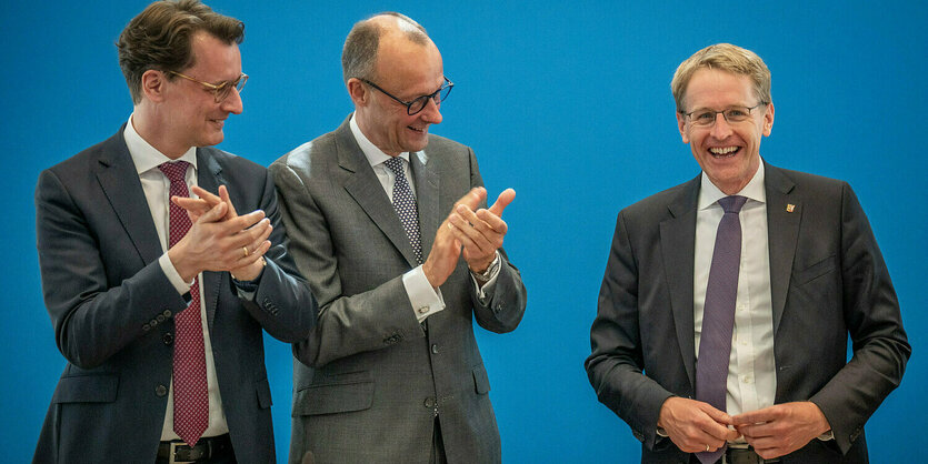 Hendrick Wüst und Friedrich Merz klatschen, Daniel Günther lacht