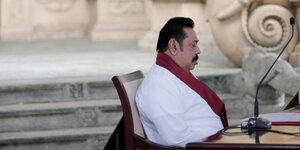 Mahinda Rajapaksa sitzt im Profil auf einem Stuhl vor einem Mikrofon