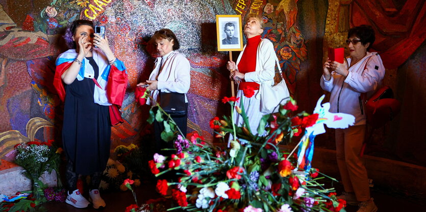 Vier Frauen, eine mit Russlandfahne stehen im Inneren der Soldatenstatuer im Treptower Park in dem sich Blumen stapeln