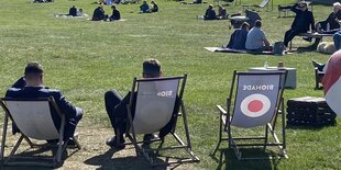 Zwei Männer sitzen in Liegestühlen auf einer belebten Wiese.