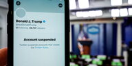 Ein Smartphone zeigt Donald Trumps gesperrten Account an, im Hintergrund ein Redepult mit US-Flagge