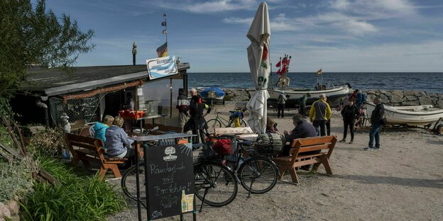 Kiosk mit Sonnenschirm und Schild "Räucherfisch" vor Ostseekulisse