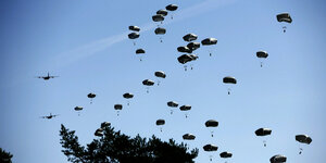 Militärische Fallschirme landen vor einem blauen Himmel