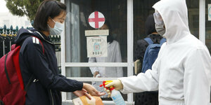 Ein Mädchen bekommt von einer Person mit Schutzanzug die Hände desinfiziert