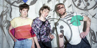 Foto der Band Painting: Die drei Bandmitglieder stehen vor einer Wand, auf sie werden Linien und geometrische Formen wie Kreise und Dreiecke per Videobeamer projiziert