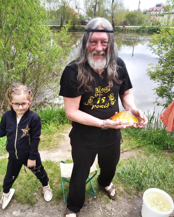 Ein älterer Mann mit langen grauen Haaren zeigt einen geangelten Fisch