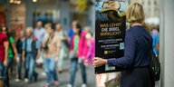 Eine Frau steht mit einem Aufsteller der Zeugen Jehovas in einer Einkaufsstraße