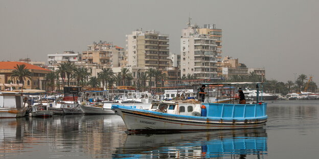 Ein Boot liegt im Wasser vor einem sand-gelb-gefärbten Himmel mit Hochhäusern. Ein Boot liegt im Wasser vor einem sand-gelb-gefärbten Himmel mit Hochhäusern.