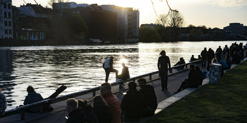 Zahlreiche Menschen genießen am Abend des Karsamstag am Ufer der Spree an der East Side Gallery den Sonnenuntergang