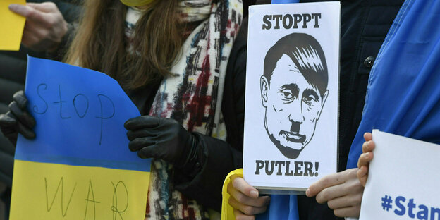 Ein Demonstrant hält ein Plakat hoch, das eine Mischung aus Putin und Hitler zeigt
