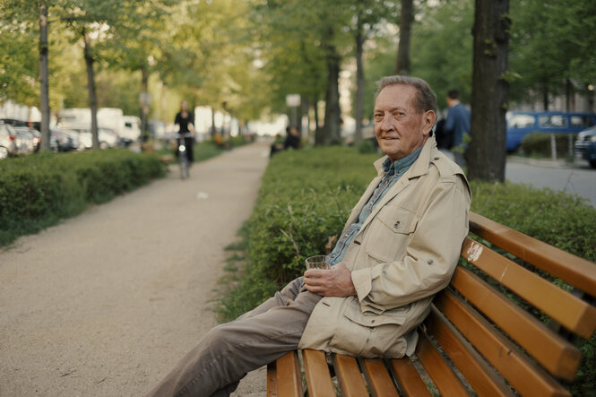 Walker sitzt auf einer Bank im Frühsommer in Berlin in der Metzerstrasse, er hält ein Whiskey-Glas in der Hand