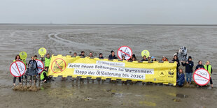 Protest mit Transparent im Watt, am Horizont klein die Bohrinsel Mittelplate