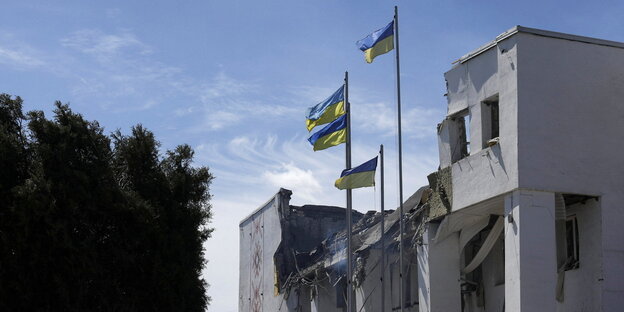 Vor einem zerstörten Haus wehen ukrainische Fahnen