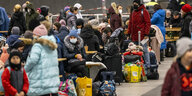 Menschen sitzen mit Koffern auf einem Bahnsteig