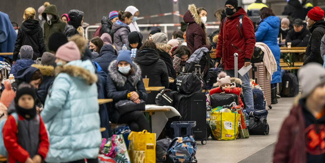 Menschen sitzen mit Koffern auf einem Bahnsteig