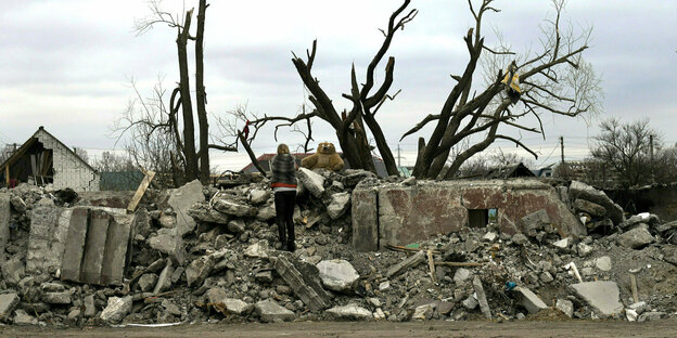 Eine Frau steht vor einem völlig zerstörten Haus