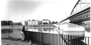 Eine Frau mit kleinem Hund schaut auf eine Brücke