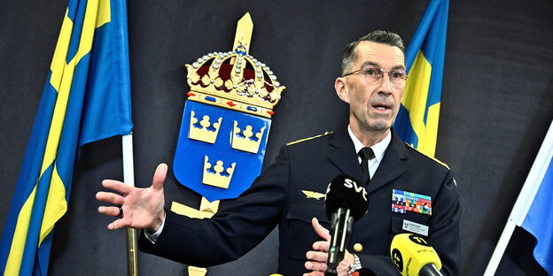 Mann in Miltiäruniform vor der schwedischen Krone und schwedischen Flagge