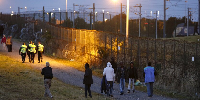 Männer laufen am Zaum zum Eurotunnel-Gelände entlang