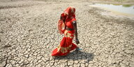 Eine Frau läuft über trockenen Boden und hält sich zum Sonnenschutz ein Tuch über Kopf und Gesicht.