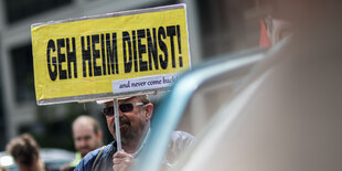 Ein Mann hält ein Schild mit der Aufschrift „Geh Heim Dienst“