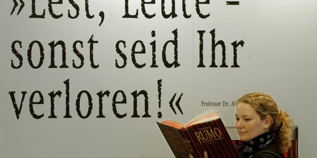 Unter dem Spruch "Lest, Leute - sonst seit ihr verloren!" blättert eine Frau auf der Frankfurter Buchmesse in einem Buch.