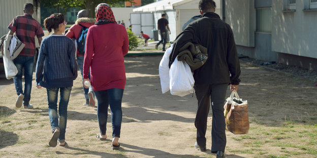 Flüchtlinge mit Bettzeug in der Hand gehen einen Weg entlang