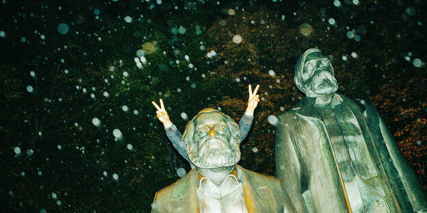 Das Victory-Zeichen zweier Hände, die hinter einer Marx-Statue hervorgucken