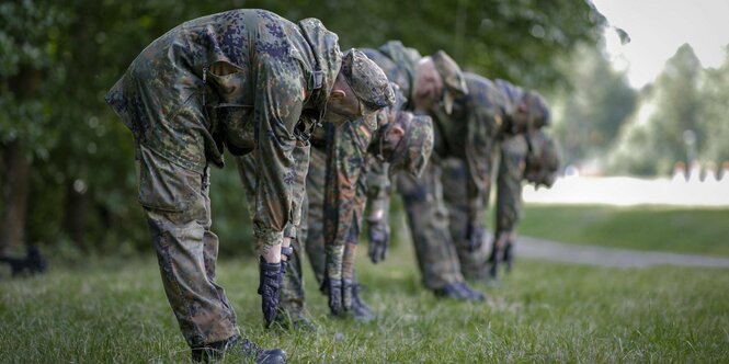 Soldaten stehen in einer Reihe und gehen mit den Händen zur Erde mit gebeugten Rücken