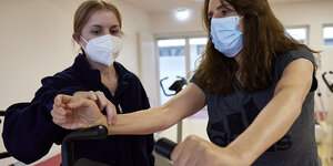 Eine Frau fühlt den Puls bei einer Patientin auf einem Sportgerät