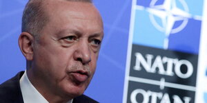 Erdogan steht vor einer mit NATO beleuchteten Wand