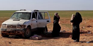 Zwei verschleierte frauen mit Kindern auf dem Arm stehen neben einem großen Auto