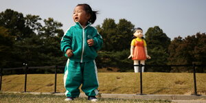 Ein Kleines Mädchen steht auf einem Feld, hinter ihr eine Puppe