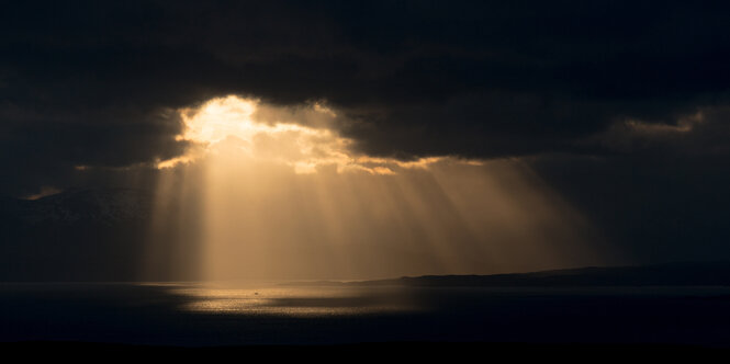 Dunkle Wolken verhängen die Sonne, letzte Strahlen auf dem dunklen Meer