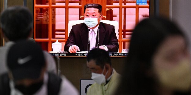 Auf einem Bildschirm sieht man Kim Jong Un mit einer Mundschutzmaske