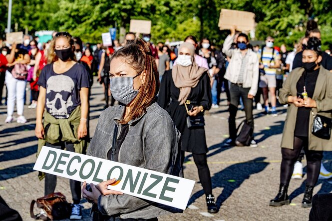 Eine Menschenmenge, eine Frau trägt ein Plakat mit der Aufschrift "Decolonize"