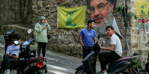 Ein Porträt von Hisbollah-Führer Narallah auf einer Mauer, davor Jugendliche auf Moped