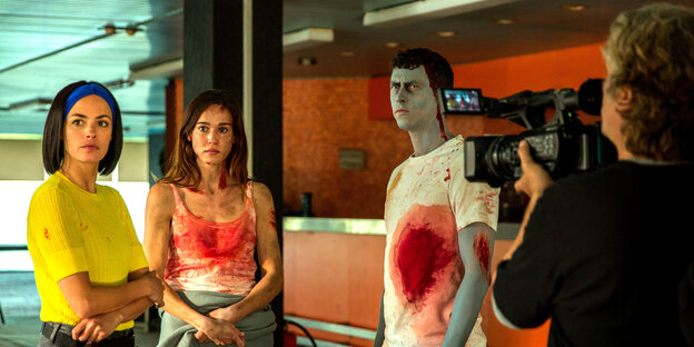 Man schaut einem Kameramann über die Schulter, der zwei Frauen und einen Mann - schon grün im Gesicht - mit reichlich Blut auf den Hemden filmt