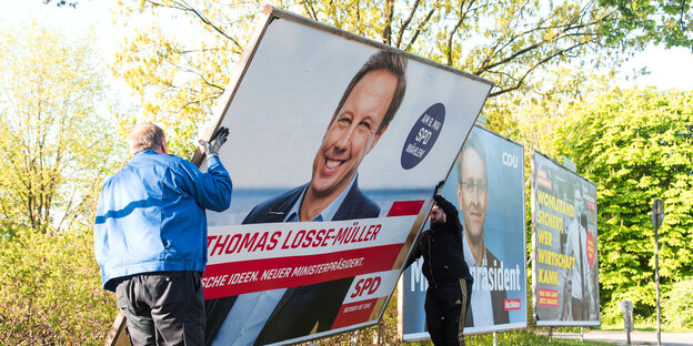Zwei Männer bauen ein Wahlplakat mit einem Foto des SPD-Spitzenkandidaten Thomas Losse-Müller ab