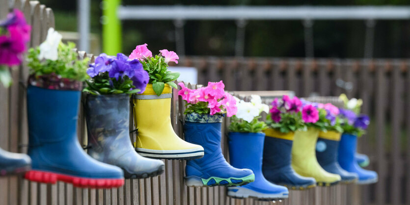 Gummistiefel von Kindern mit Blumen hängen am Zaun eines Kindergartens in der Region Hannover.