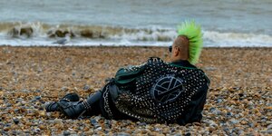 Ein Punk mit bunten Haaren auf dem Kopf liegt am Strand