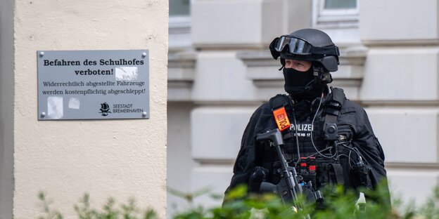 Ein Polizist mir Helm und Waffe steht vor dem Eingang der Schule in Bremerhaven