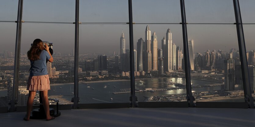 Eine junge Frau sieht durch ein Fernglas auf die Türme im Marina District in Dubai